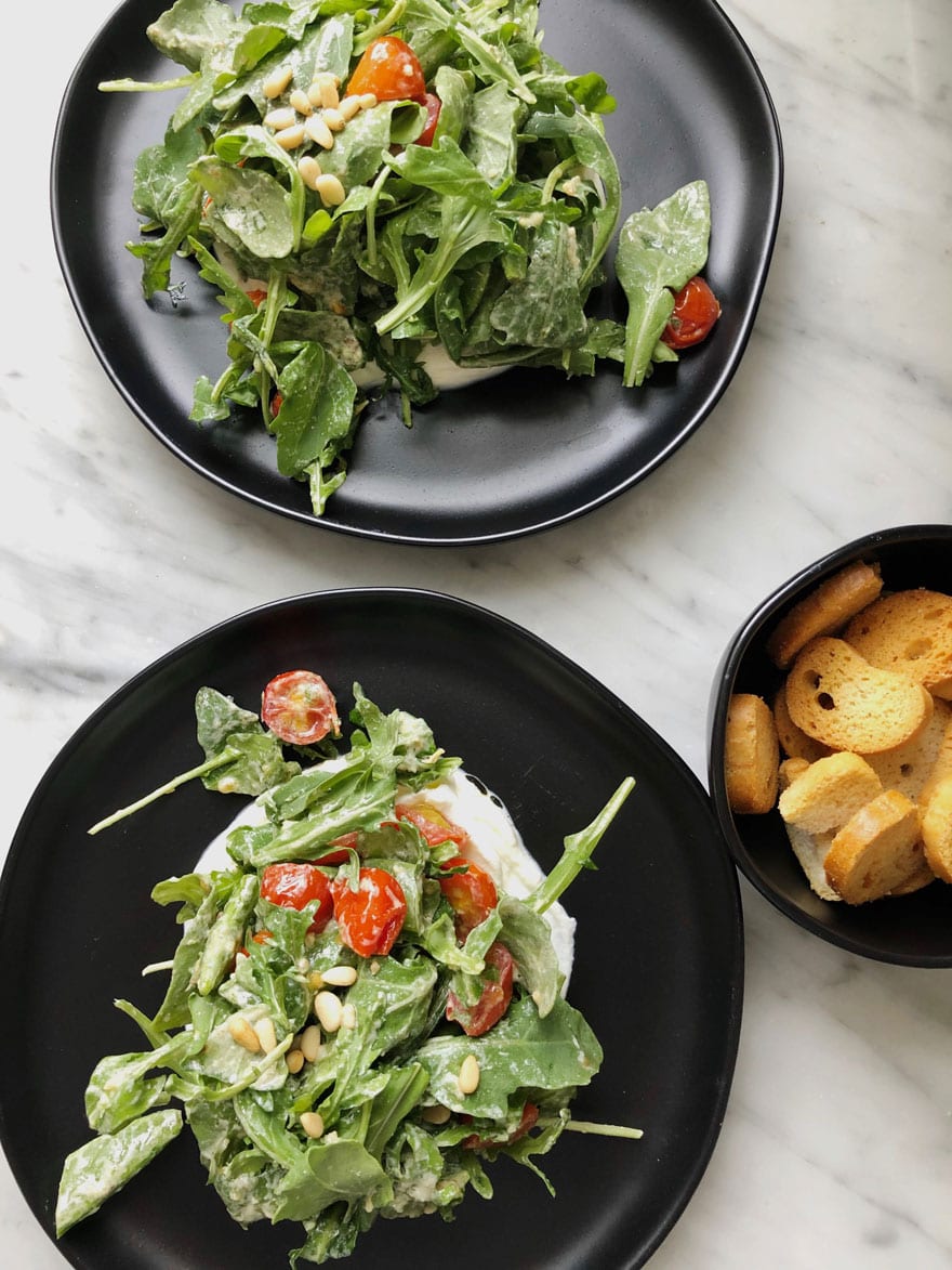 salad on black plates with small black bowl of tiny toasts