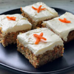 carrot cake squares with X made out of carrot shreds for decoration on black plate