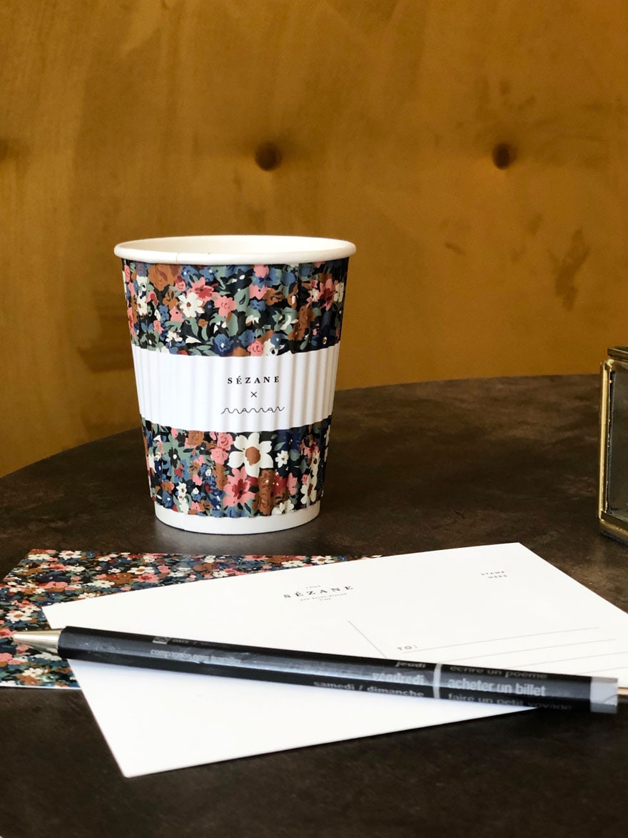 a patterned coffee cup and post cards with a pen on a table with a gold velvet bench 