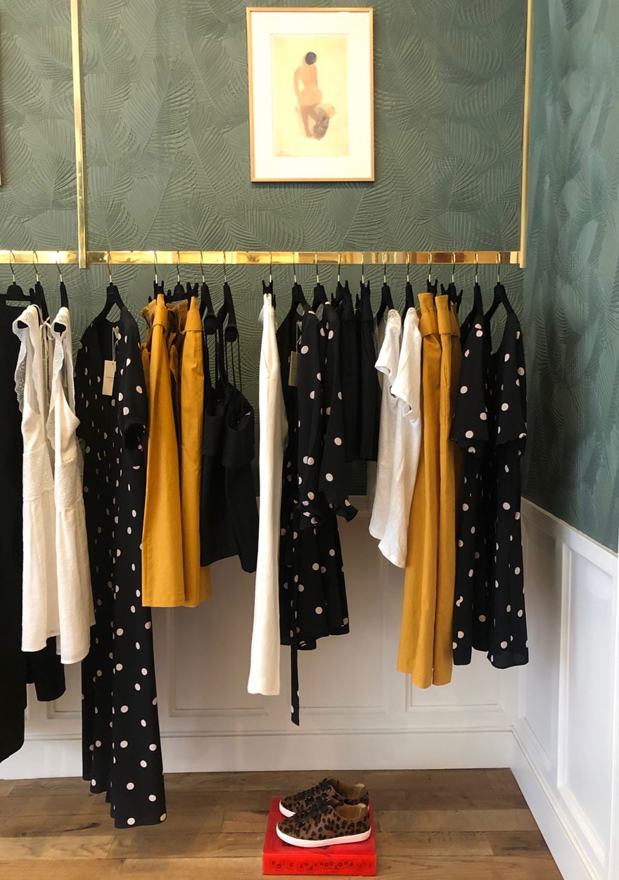 black and gold and white clothing pieces hanging from a brass bar against a green textured wall above white