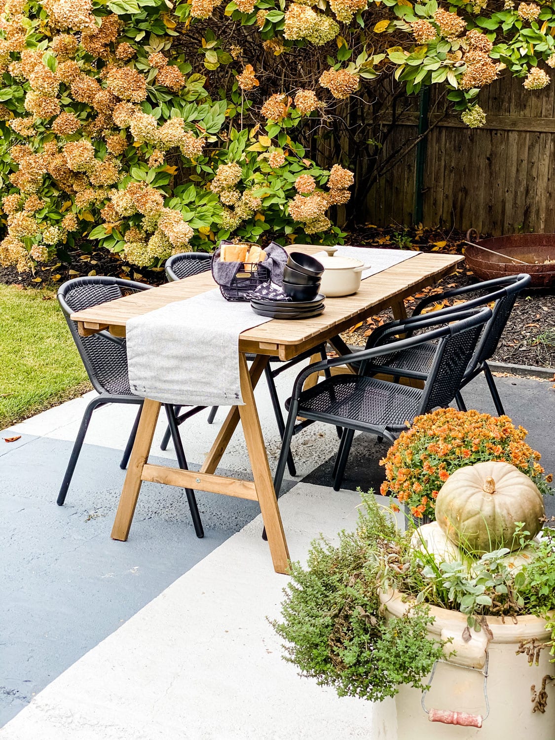 an outdoor table with black dishes and basket of bread with hydrangeas in background