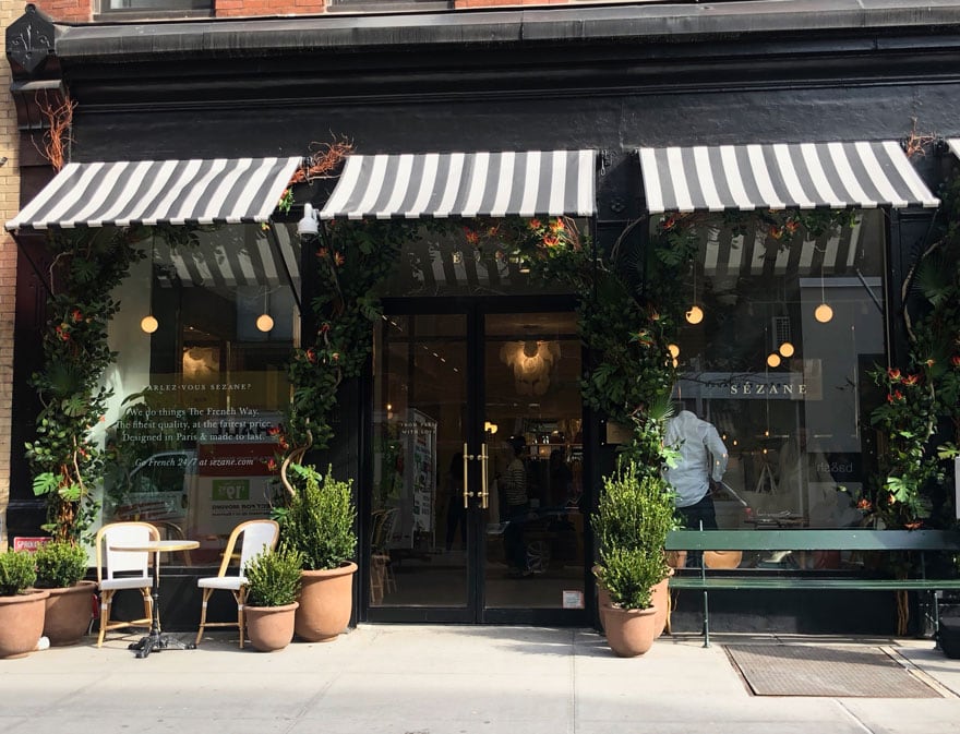 storefront painted black with black and white awnings, potted trees, cafe chairs