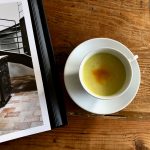 cup with gold drink on wood table with book page open