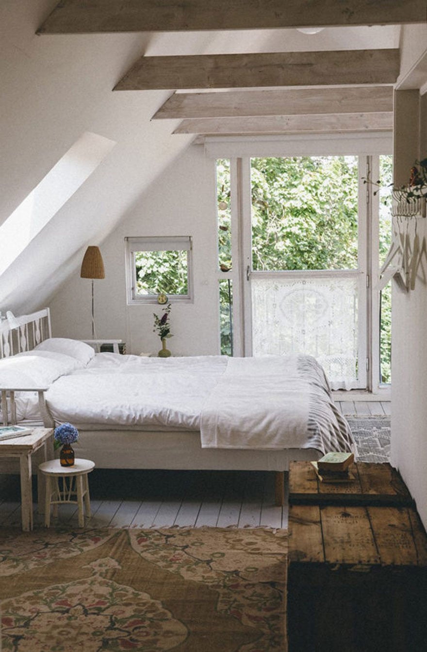 A gorgeous attic space in a home in Southern Sweden. The floors, walls, and ceiling are painted white and the bare beams and floors are natural.