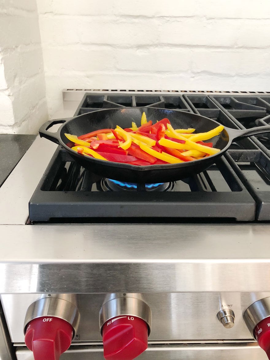 red and yellow peppers cooking in skillet over gas heat