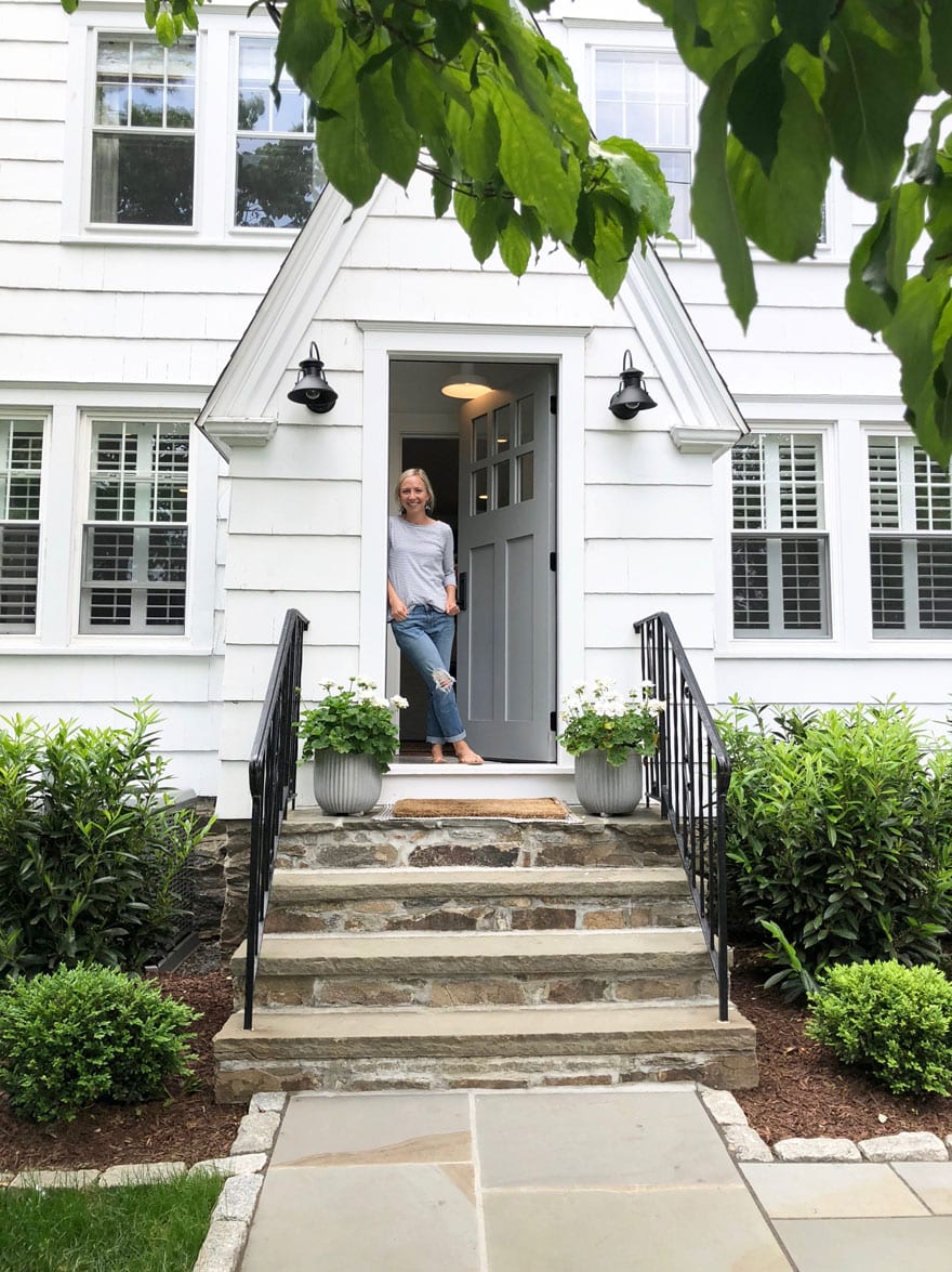 woman standing in door way of white house with gray door