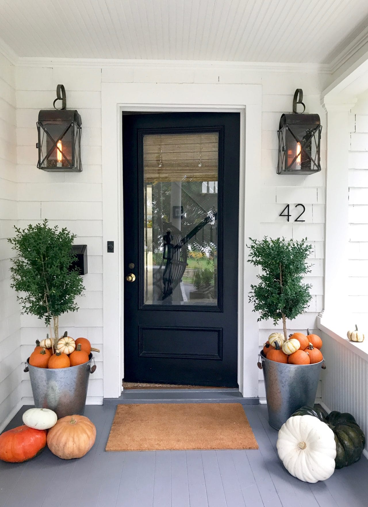 white house with black door with planters and pumpkins 