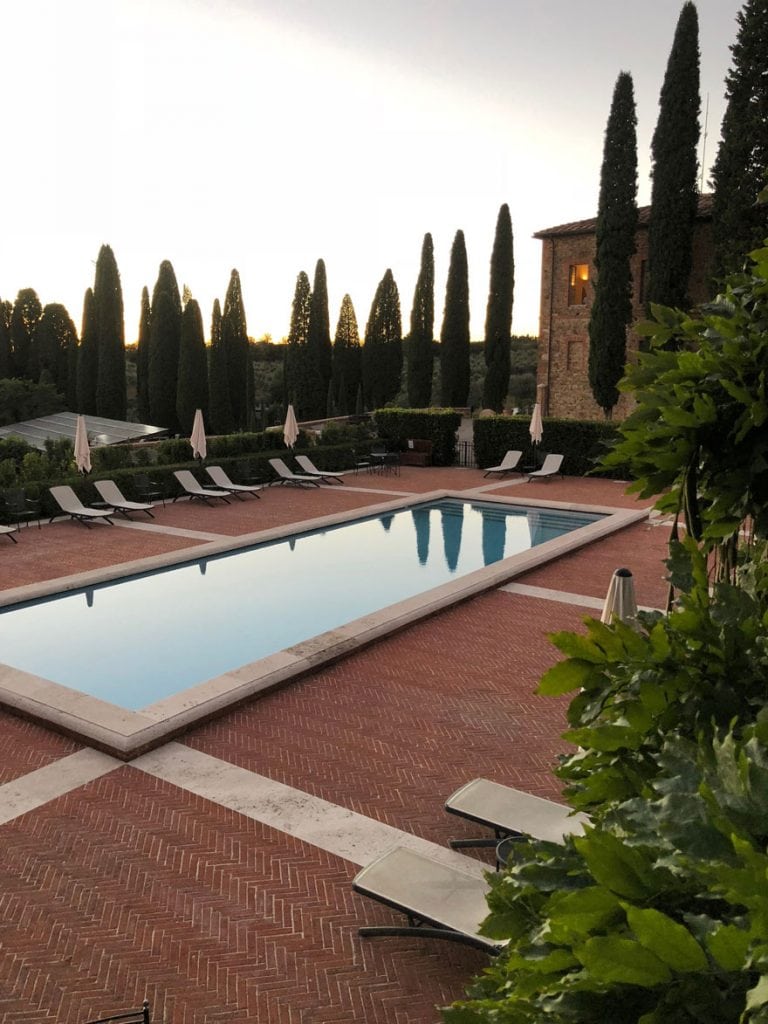 Rectangular swimming pool with Italian Cypress trees and red brick deck.