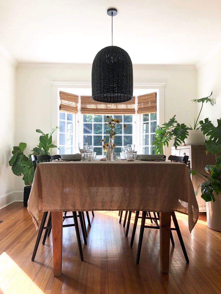 table and chairs with tablecloth and large blaclk pendant in room with large window