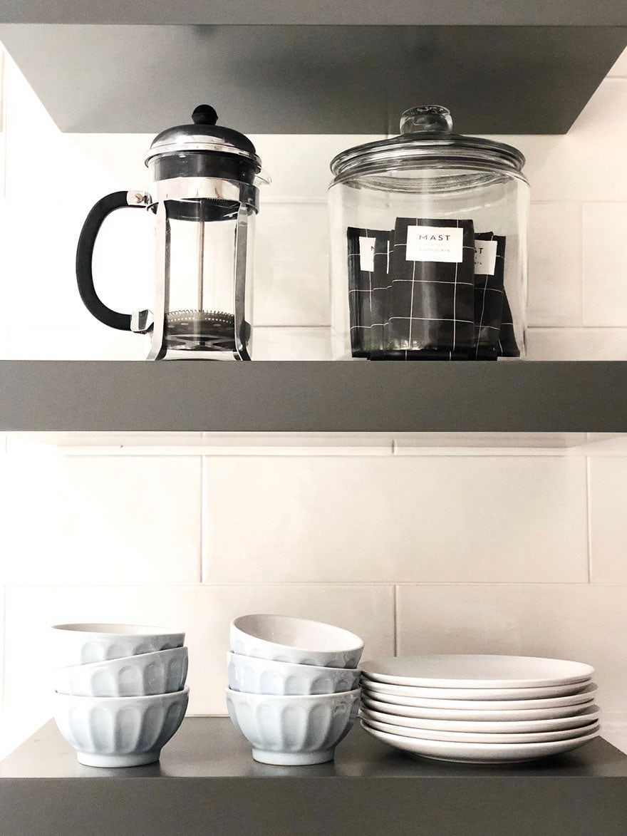 shelves with jar of candy bars, small latte bowls, coffee press, plates