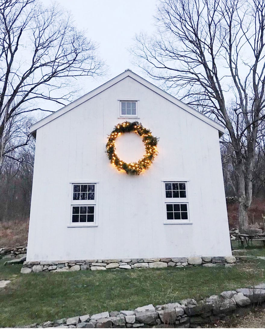 white barn with wreath with lights