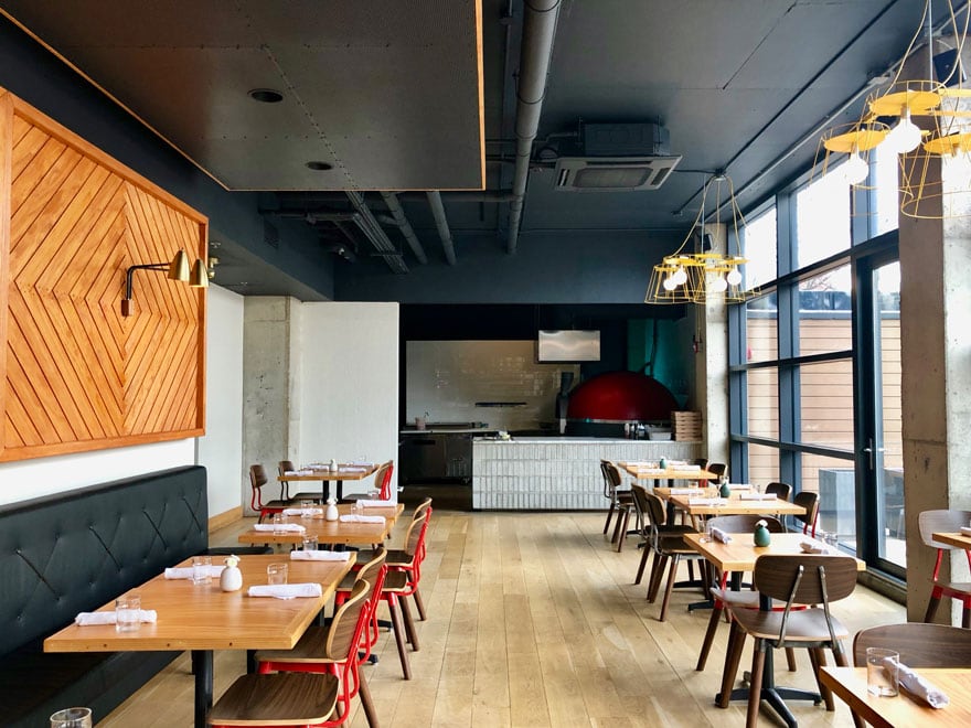 restaurant interior with red chairs, tables, pizza oven, wood floors, windows