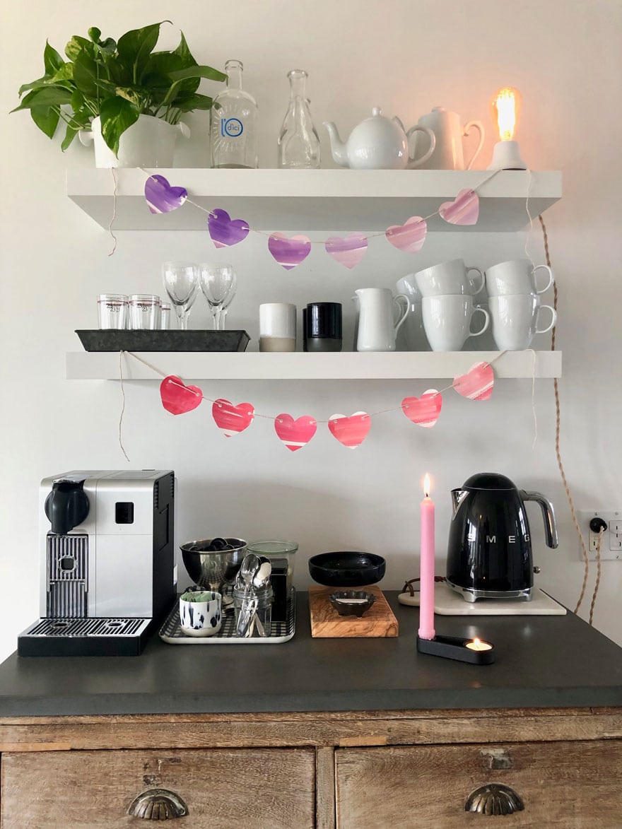 coffee bar with heart garland, cups, glasses, tea pot, coffee maker, candle