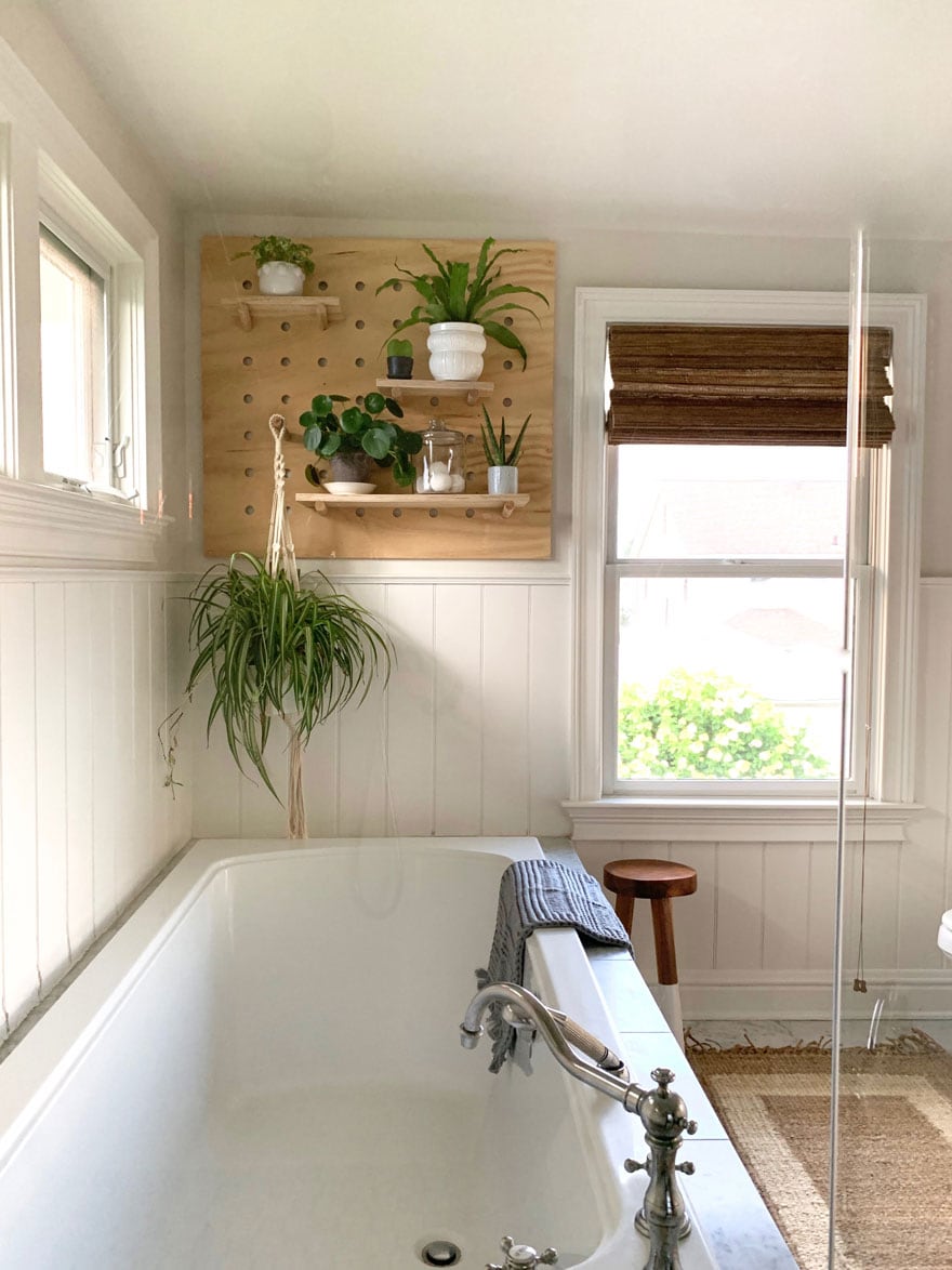 bathroom tub and window with stool, pegboard with plants