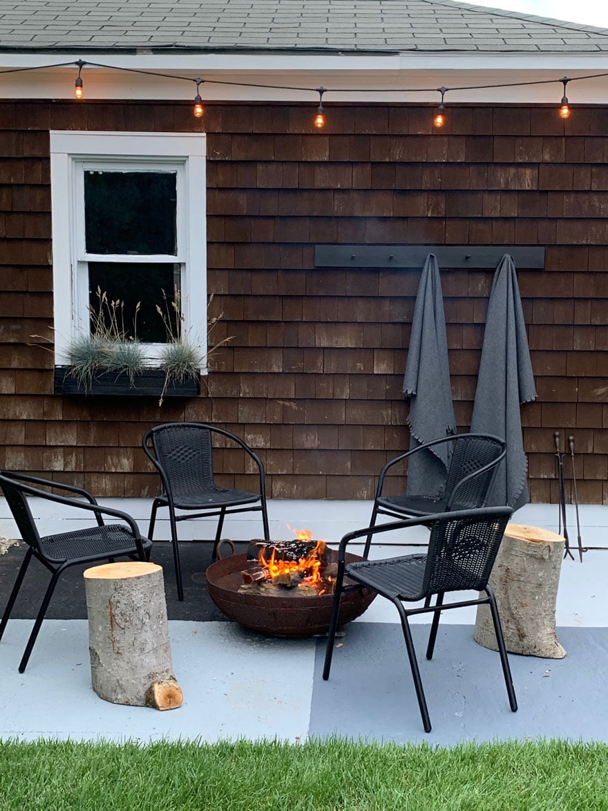 chairs, fire pit, tree stumps, window, throws on hooks on side of garage