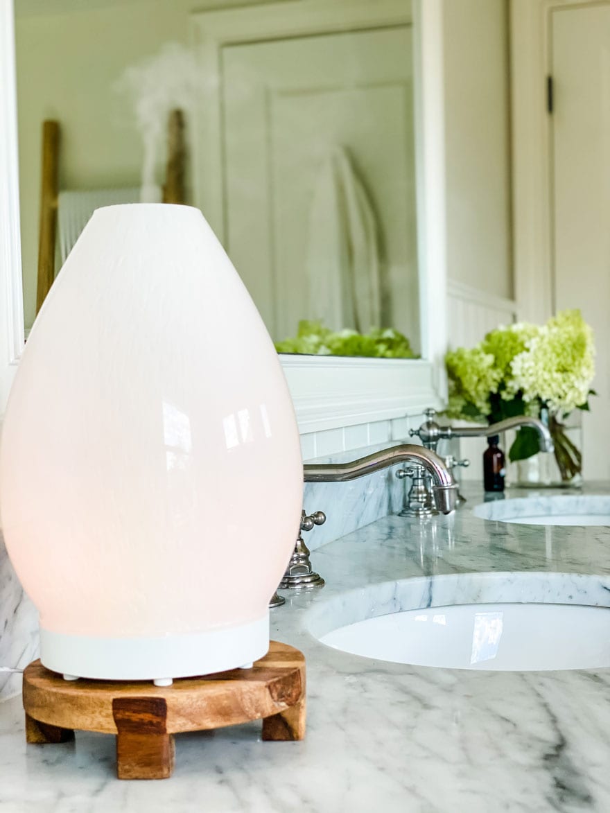 Lifestyle blogger Annie Diamond shows her new Lustre diffuser on a wood trivet on her marble bathroom vanity