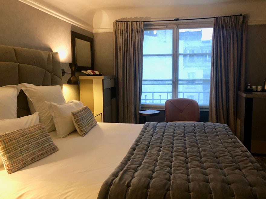 bed in hotel room with velvet comforter and pillows, window