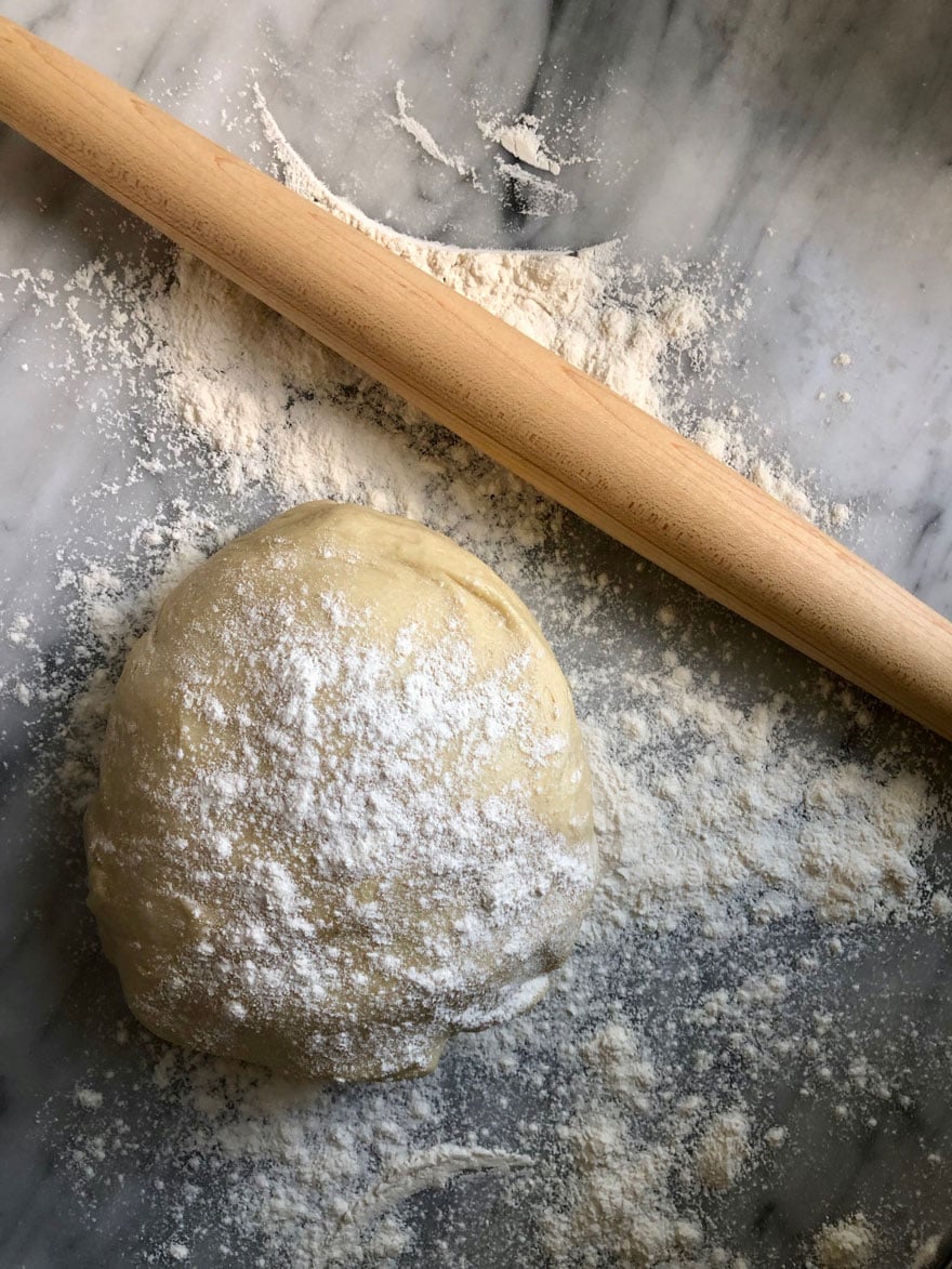 dough dusted with flour, french rolling pin on marble counter