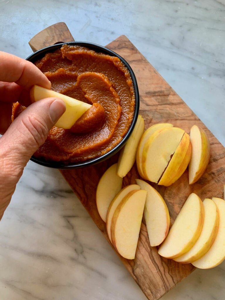 Apple slices are on a small, wooden dessert board served with with tasty homemade pumpkin butter.