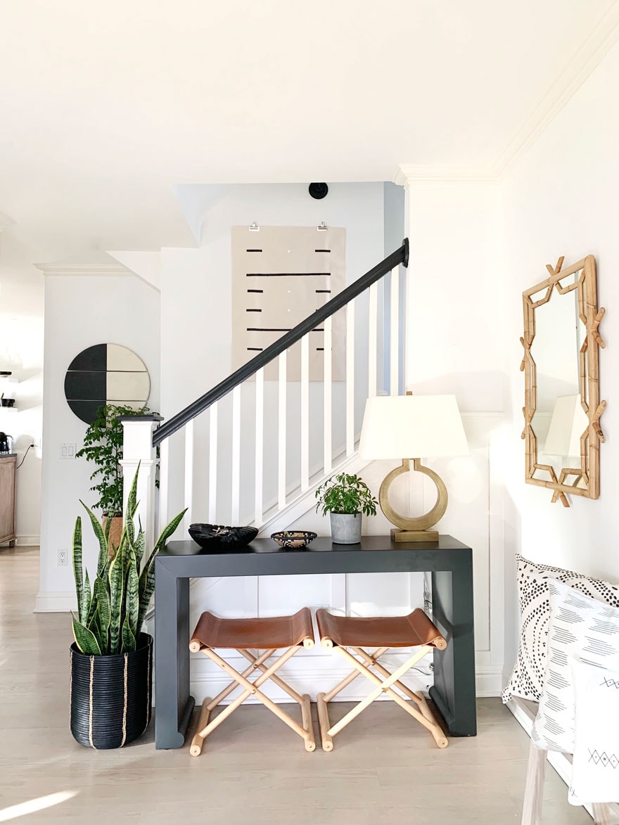 an entryway with a console table, lamp, 2 stools and mirror, snake plant