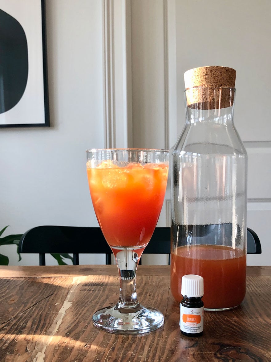 red orange drink on table with glass bottle and bottle of essential oil