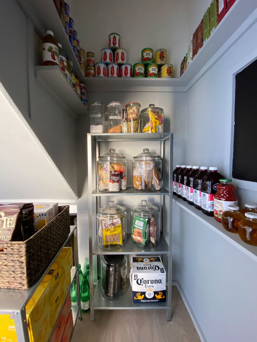 a metal shelf against a gray wall with hardwood floors in a pantry with food and jars of food