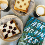 copy of book, Ask Again, Yes and coffee cups and toast on plates on marble table top
