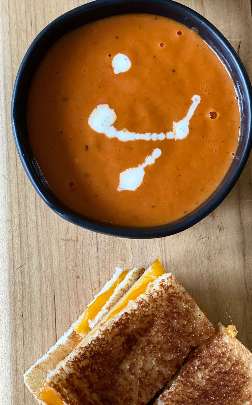 small black bowl of tomato soup with grilled cheese on wood board