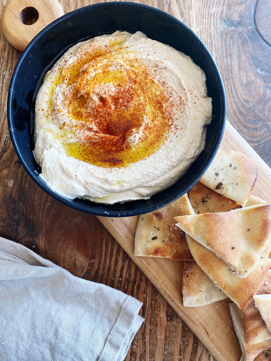 hummus in black bowl on wood board with pita chips