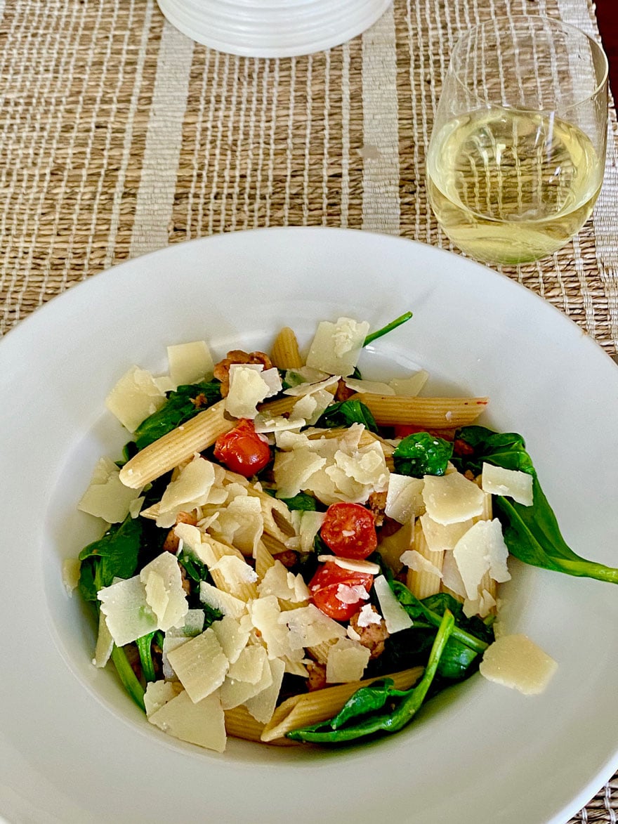 white bowl with pasta, spinach tomatoes and a glass of white wine