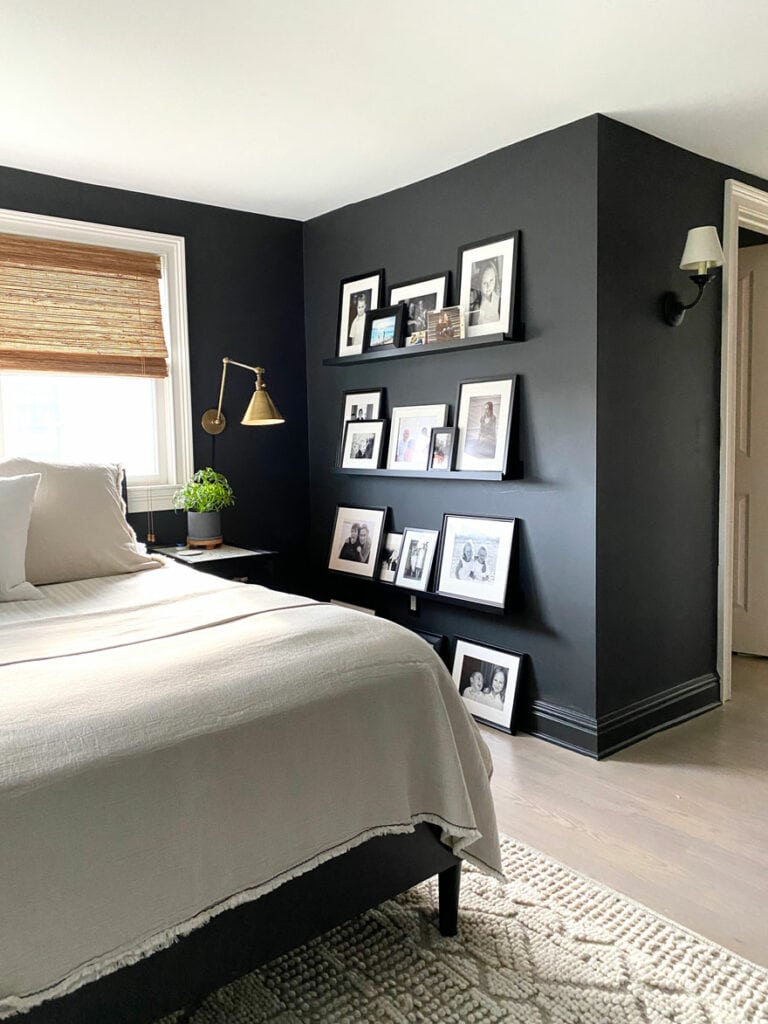 corner of bed in black room with brass sconce and photos on ledges