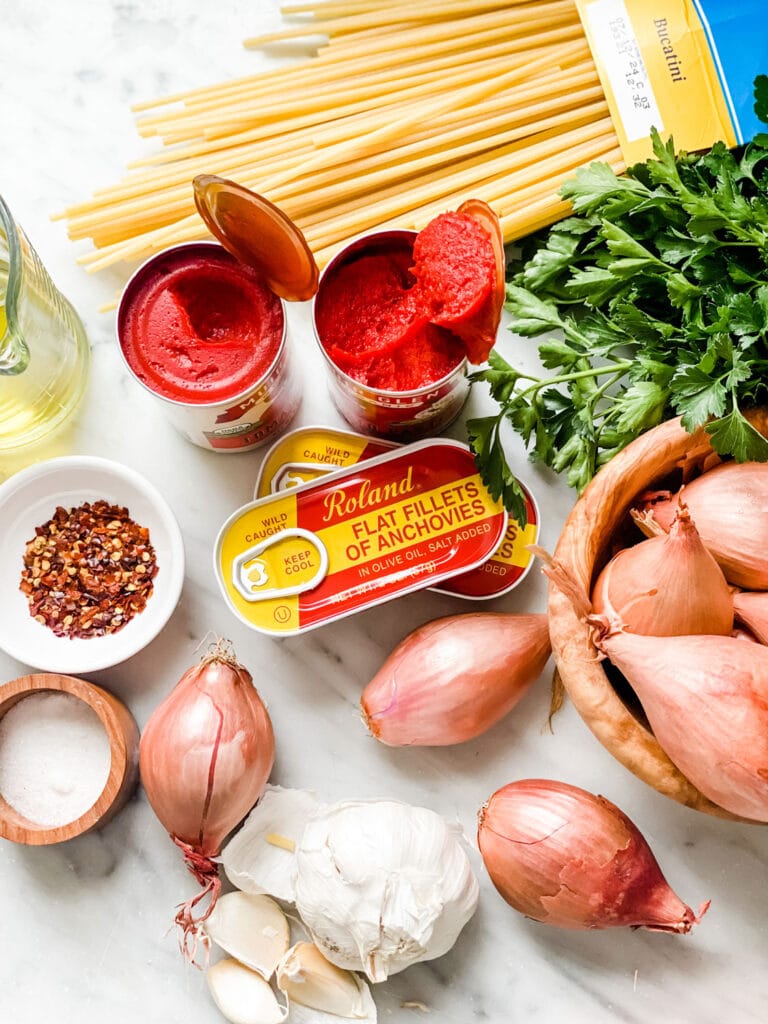 ingredients on marble counter, pasta, tomato paste, shallots, anchovies in cans, parsley