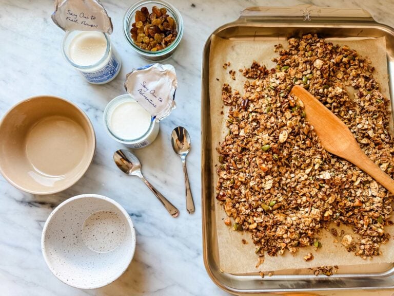 Easy homemade granola is on a baking sheet next to bowls and containers of yogurt.