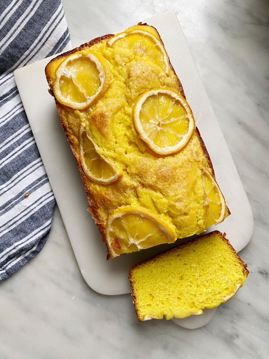 Lemon cake on white marble board with striped dish towels.