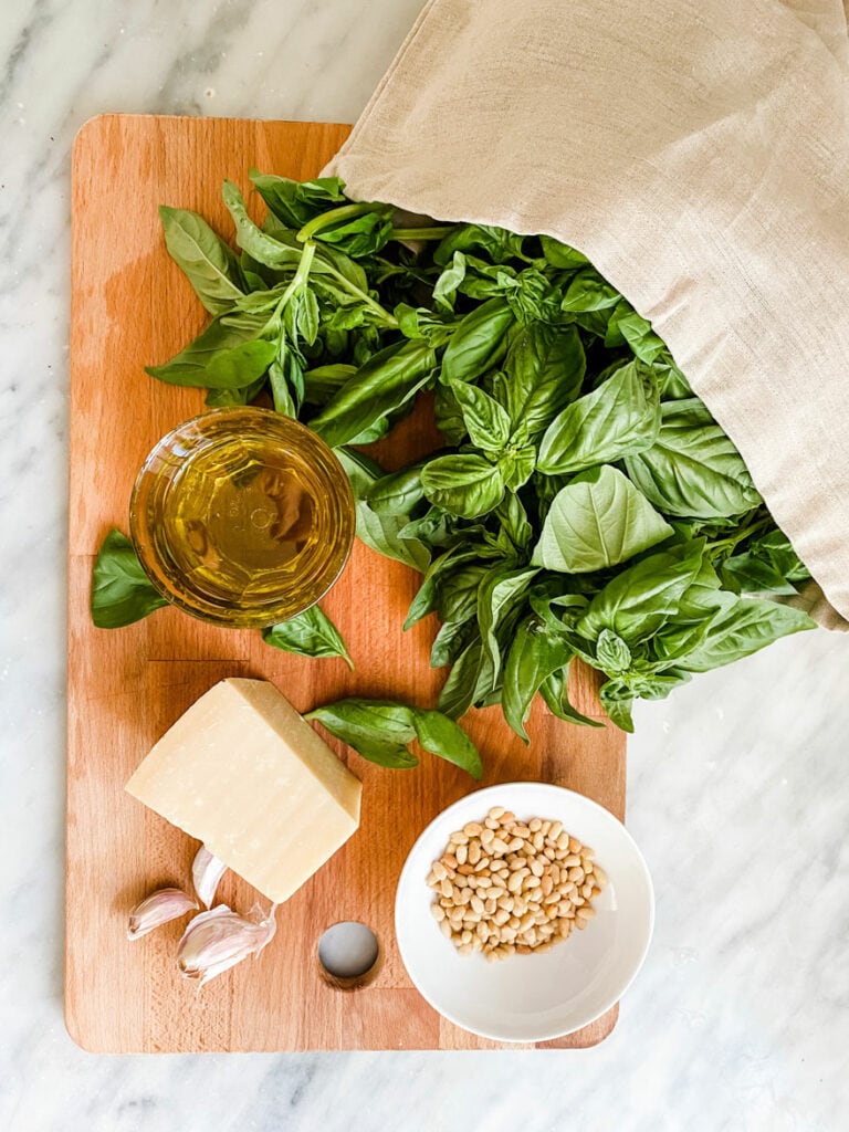 Ingredients for basil pesto on a wood cutting board.