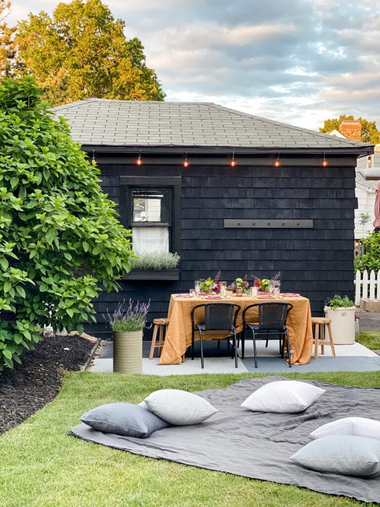 black garage with string lights and table set up with gold cloth, pillows in the yard