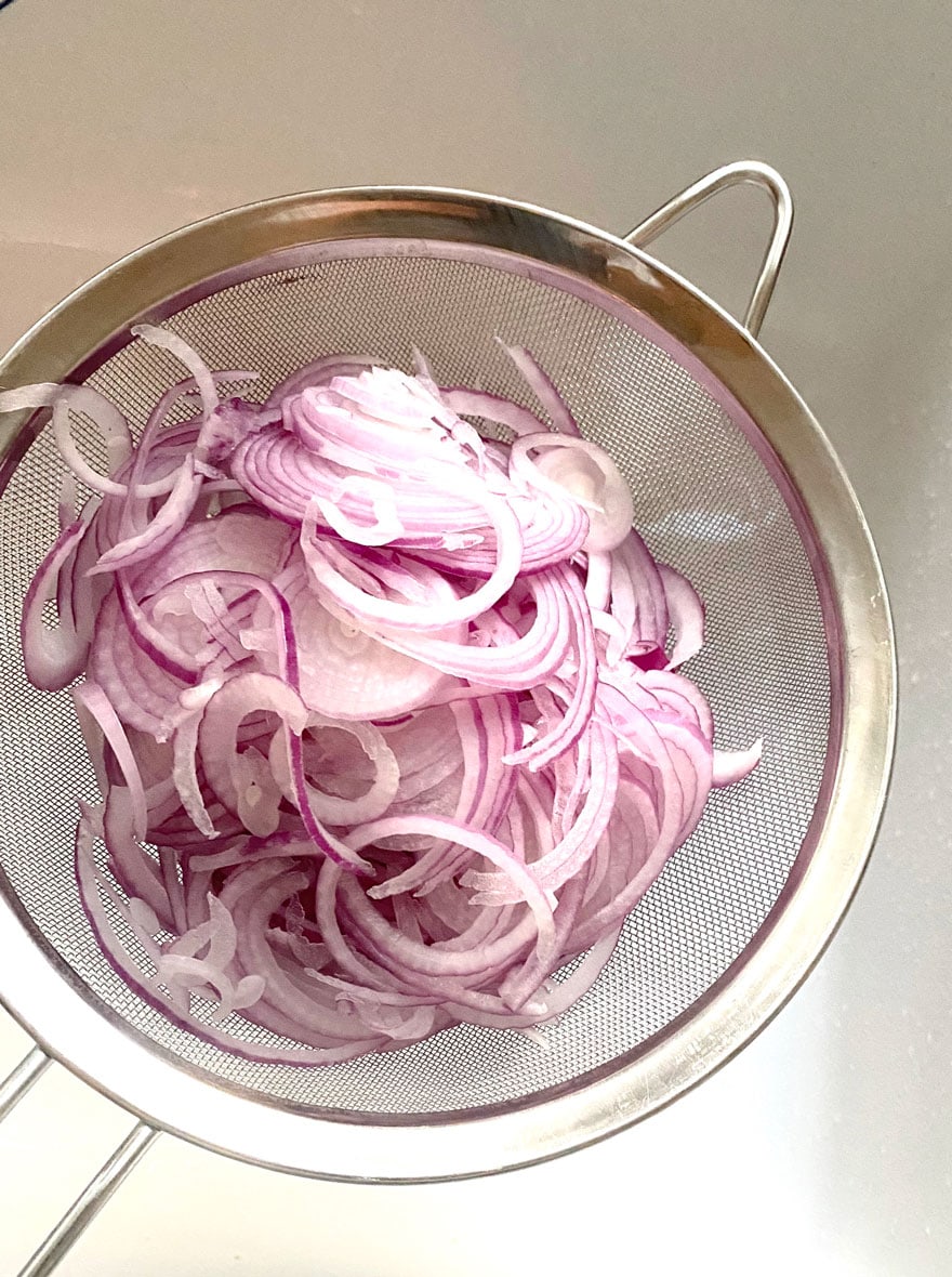 sliced red onions in mesh strainer over sink