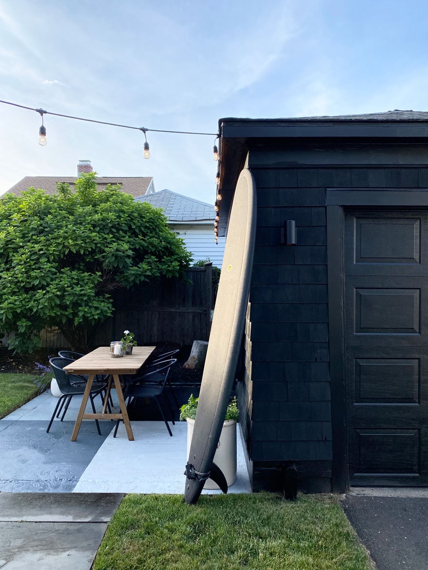 black surf board leaning against a black garage of a beach house