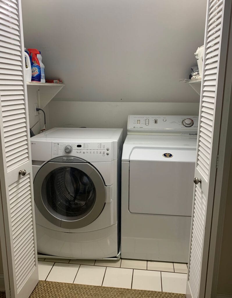 A washer and dryer are in a laundry closet with bifold doors open before the homeowner did a complete laundry room remodel.