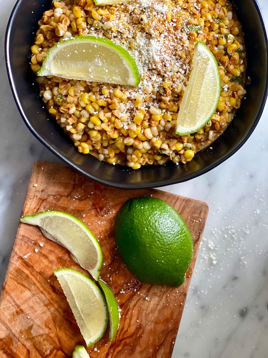 skillet with corn and limes on a wood cutting board
