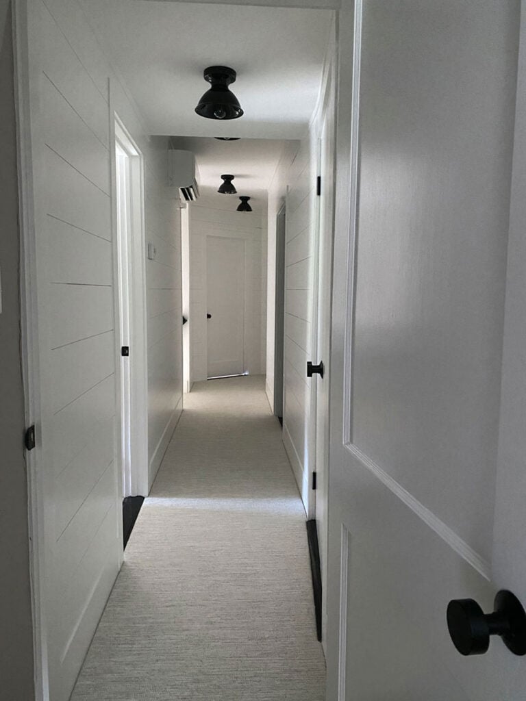 A white hallway with black Emtek hardware on all the doors and black surface mount lights on the ceiling. A Mitsubishi air conditioner has also been installed in the hallway.