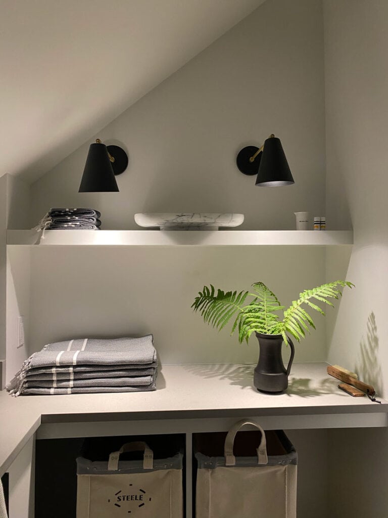 2 black sconces over a white shelf, taels fern in a black pitcher, and a marble tray on the shelf.