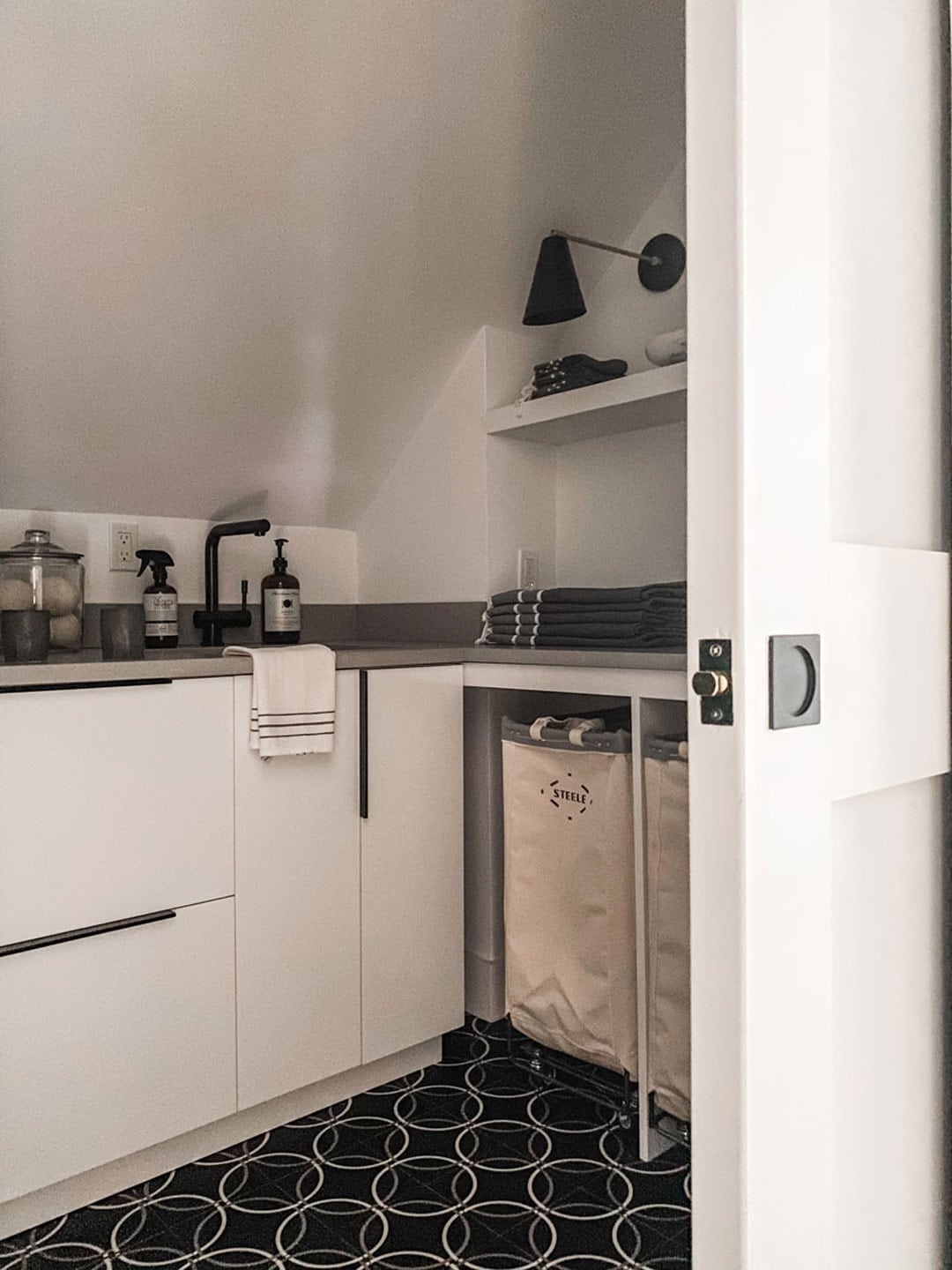 white cabinets, sink, laundry bins. sconce