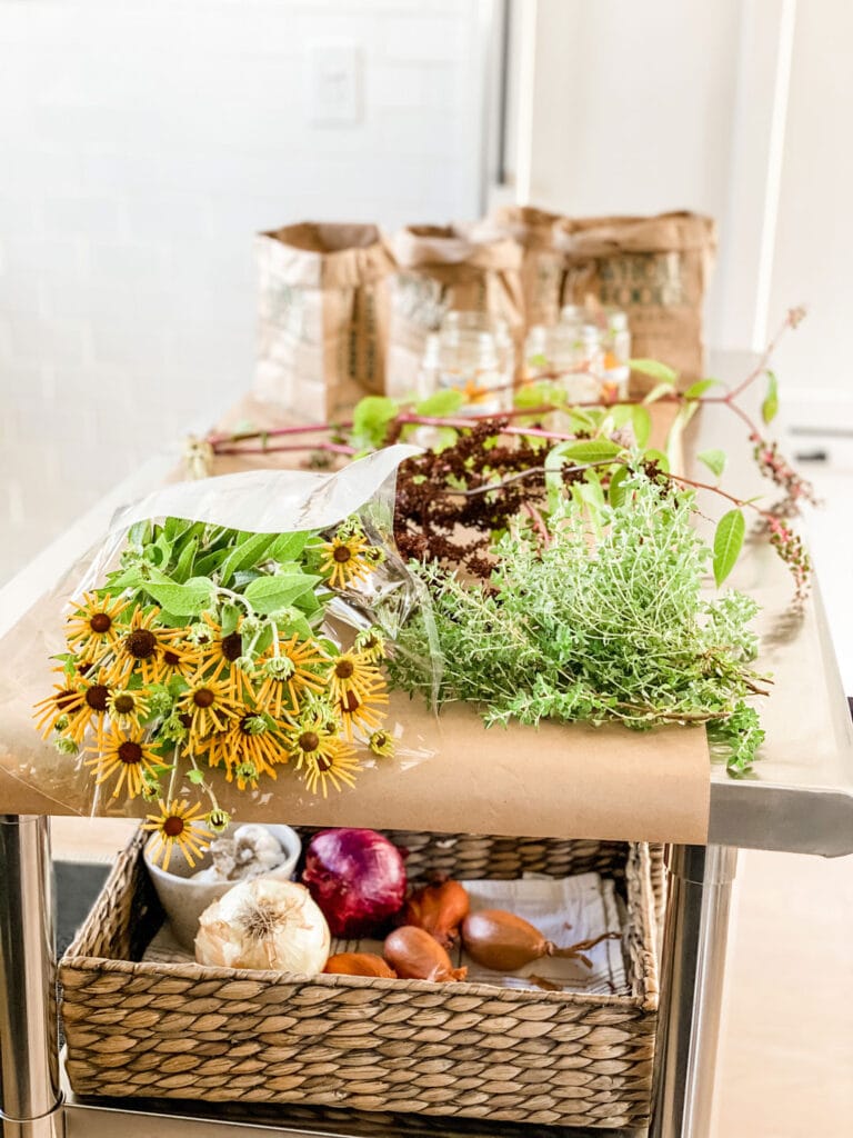 Store-bought flowers, herbs, foraged flowers, glass jars and brown paper bags sitting on kitchen island.