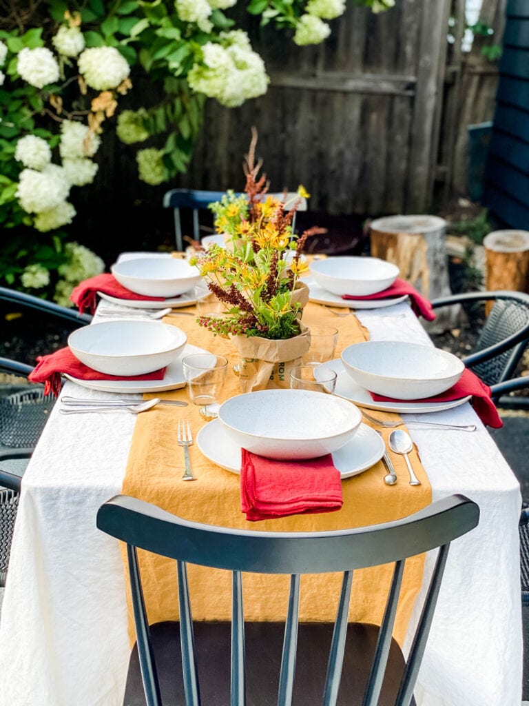 Outdoor table with colorful linens, black chairs, and rustic floral arrangements run down the center of the table.