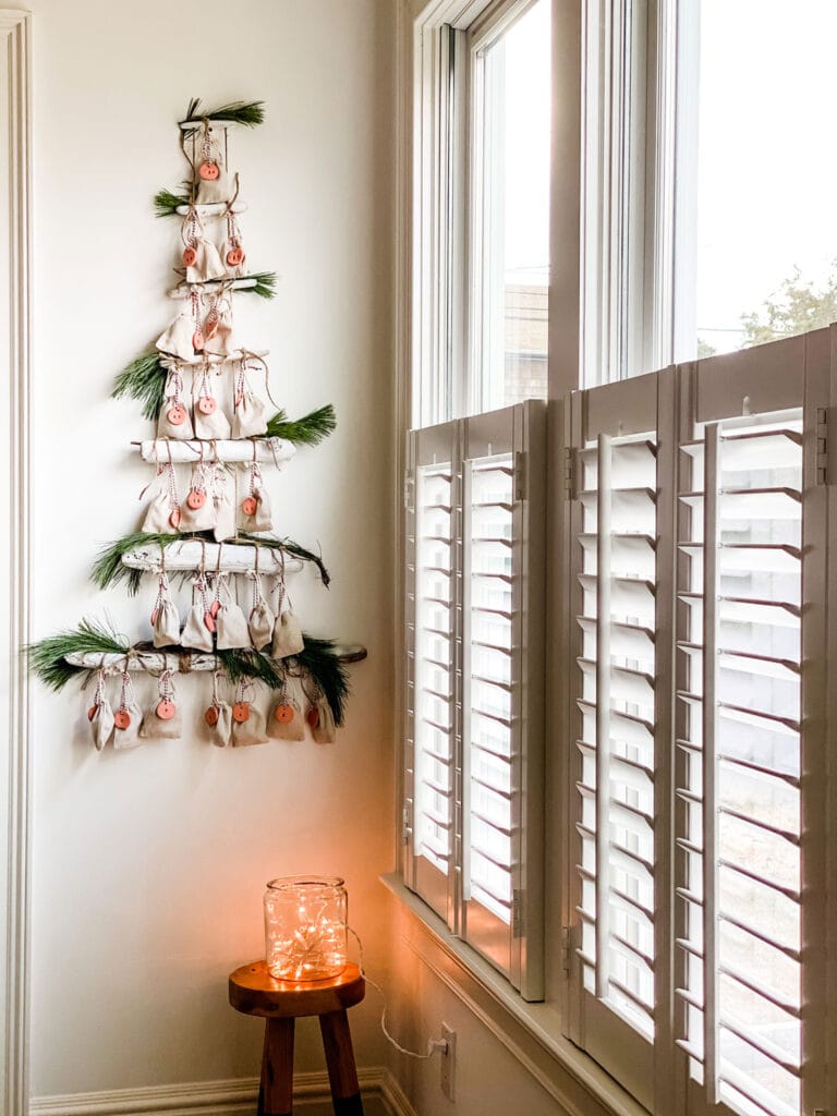 driftwood, greens, bags, clay tags advent calendar on white wall by a window