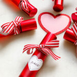 Red roller bottles with ribbon and heart shaped label around a pink/red glitter heart