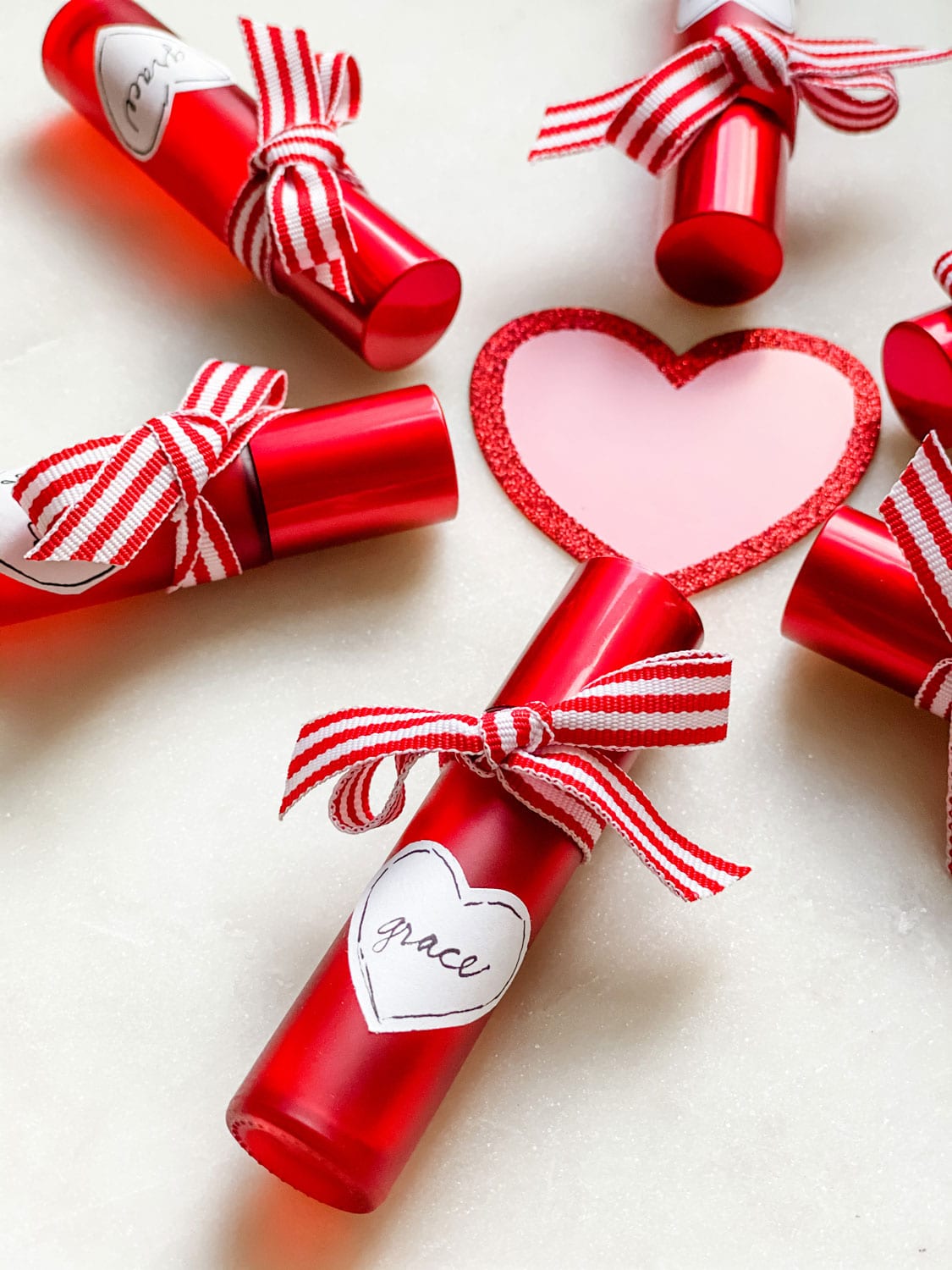 Red roller bottles with ribbon and heart shaped label around a pink/red glitter heart