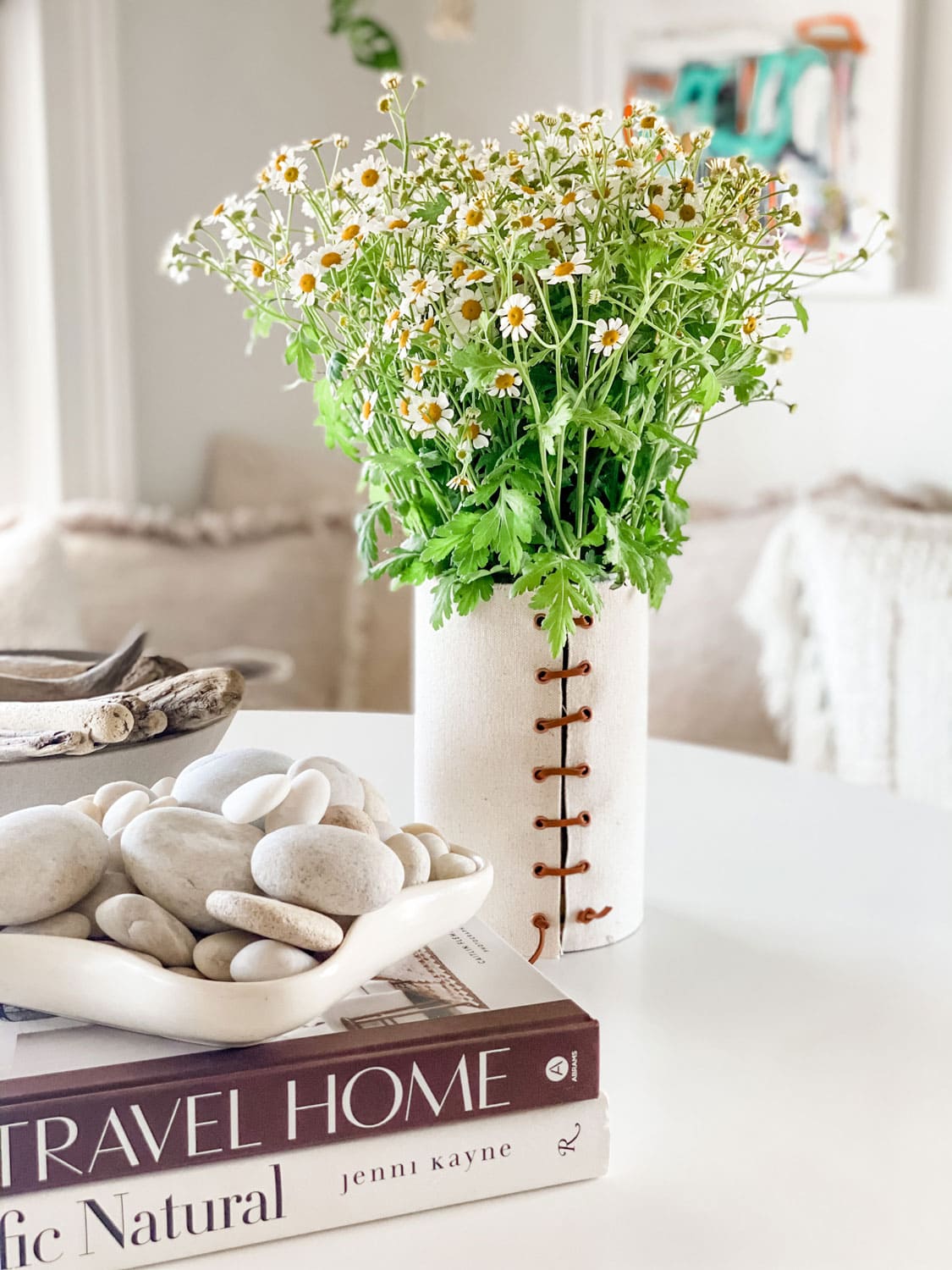 vase with chamomile, books and rocks/driftwood on white table