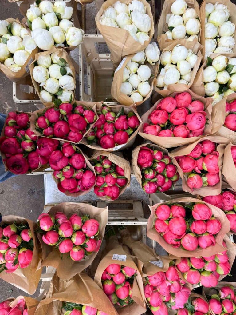 Various shades of pink and white peony are wrapped in brown paper at this storefront.